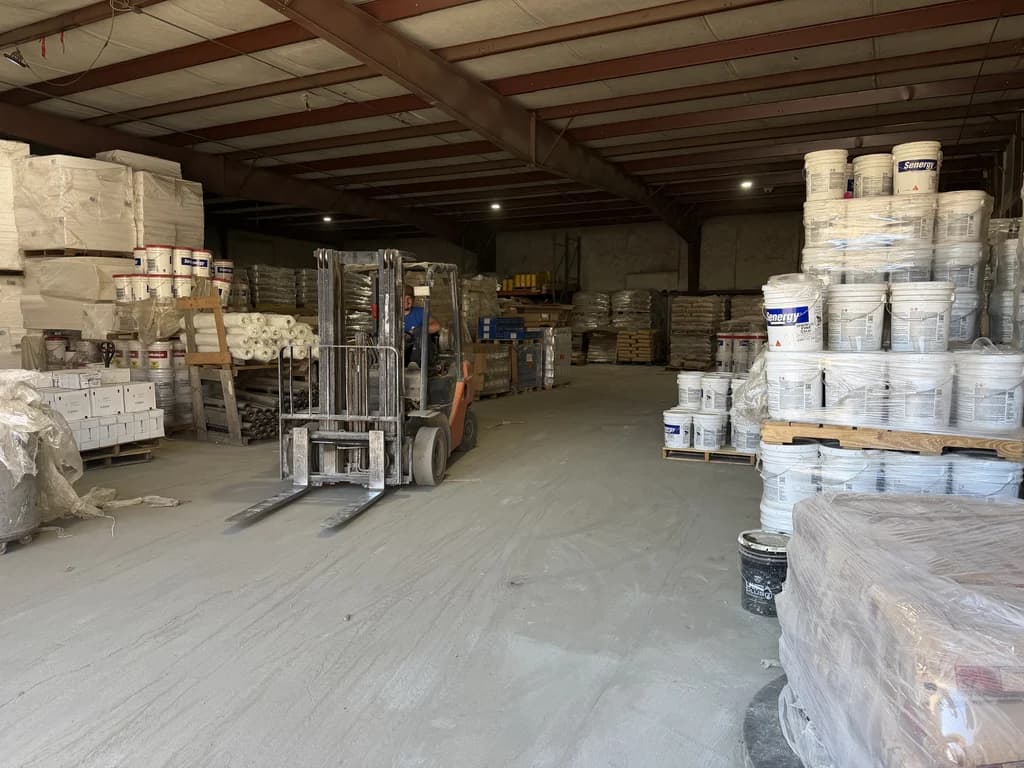 Dentro de la bodega de Best Building Materials en Suwanee: un montacargas entre tarimas de cubetas Senergy y materiales de estuco